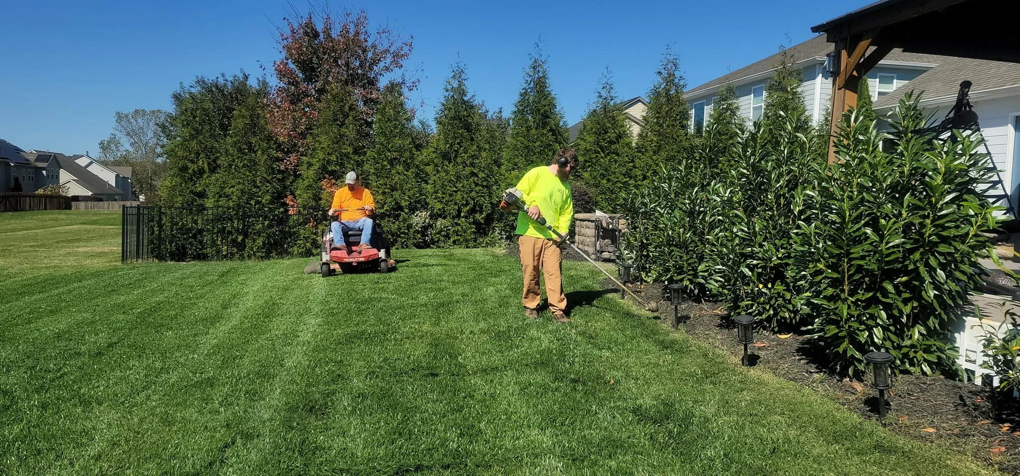 Crew mowing and trimming a large green lawn